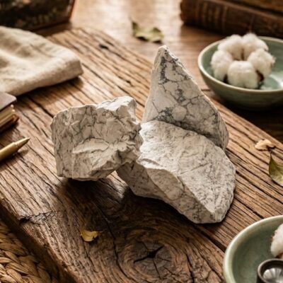trois pierres de howlite blanche avec des lignes grises posées sur un fond en bois entourées de fleurs de coton