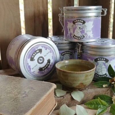4 boites de thé de la marque Alveus et une tasse de thé vert avec des fleurs blanches et vertes et près d'un livre, posées dans une caisse en bois