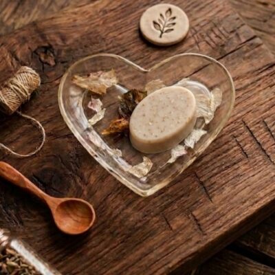 Un savon ovale sur une coupelle en forme de cœur en résine époxy avec des inclusions de fleurs séchées. Posé sur une table en bois