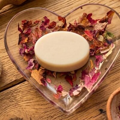 Un savon ovale sur une coupelle en forme de cœur en résine époxy avec des inclusions de fleurs séchées. Posé sur une table en bois