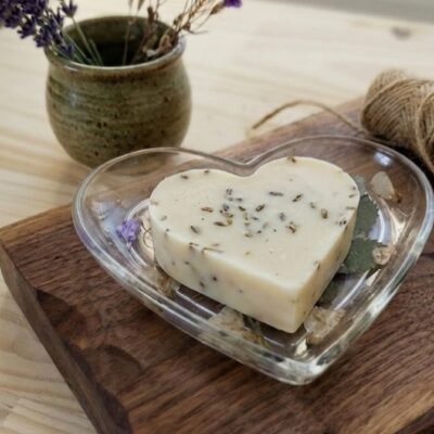 Un savon en forme de cœur sur une coupelle en forme de cœur en résine époxy avec des inclusions de fleurs séchées. Posé sur une table en bois