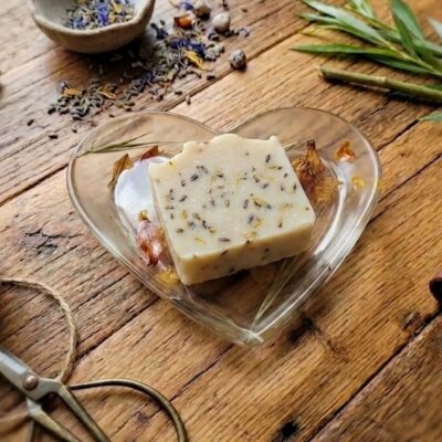 Un savon carré sur une coupelle en forme de cœur en résine époxy avec des inclusions de fleurs séchées. Posé sur une table en bois