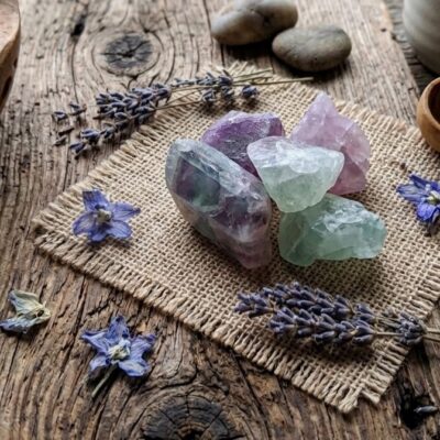 cinq pierres de fluorite vertes, violettes sur un carré de jute sur un fond en bois entourées de fleur de lavande et de fleurs violettes