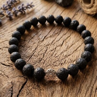un bracelet en pierre de lave noir de 8 mm, posé sur un fond en bois et entouré de fleurs de lavande