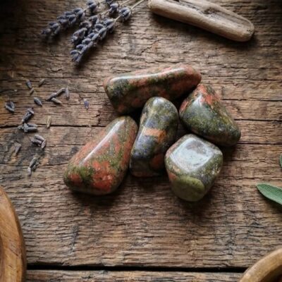 cinq pierres d'unakite vertes et oranges sur un fond en bois, entourées de feuille de sauge, de fleurs de lavande et de sel dans une coupelle couleur or